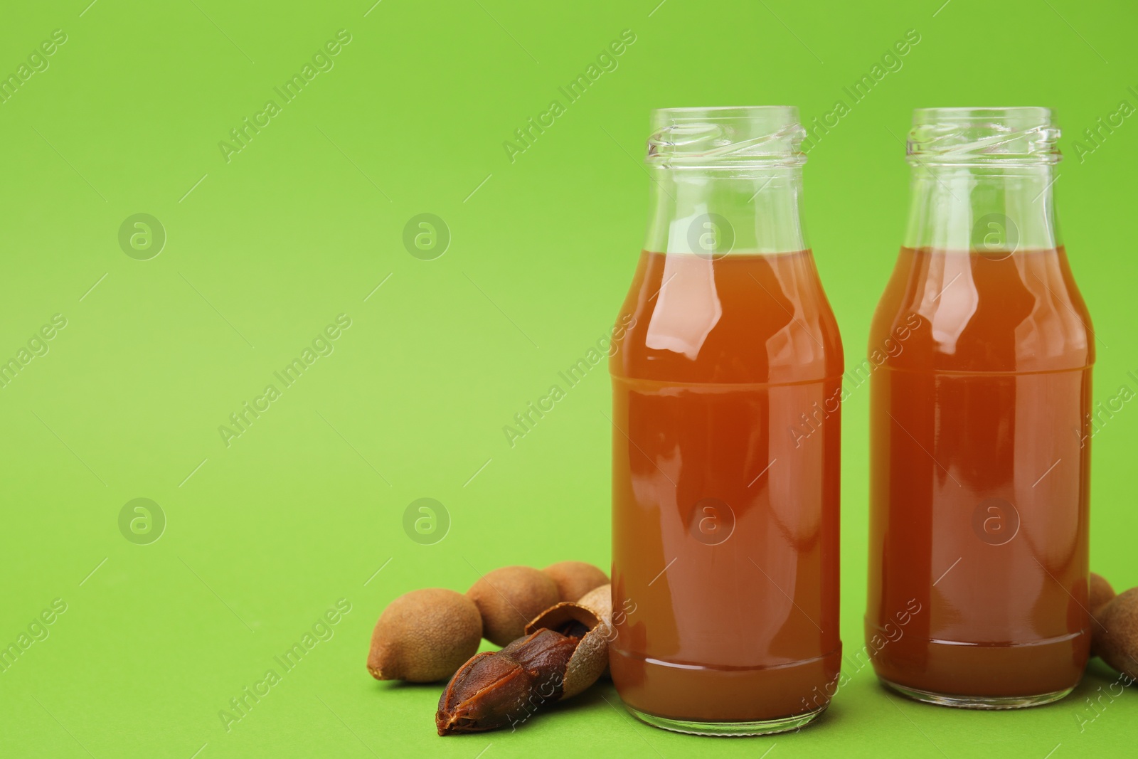 Photo of Tamarind juice and fresh fruits on green background, space for text