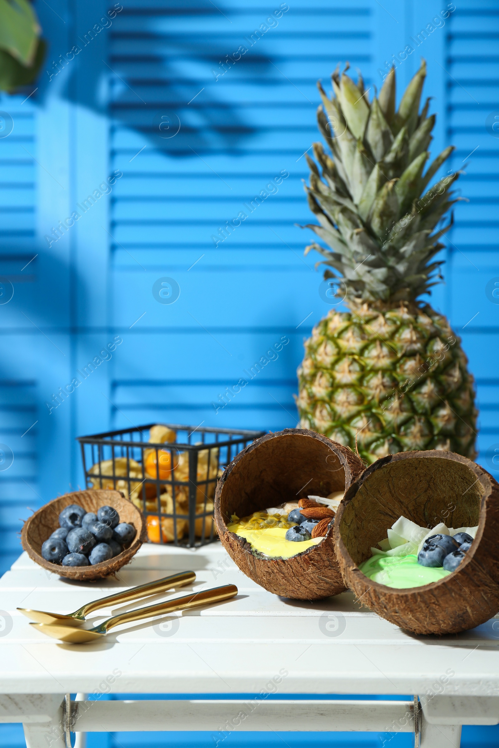 Photo of Tasty smoothie bowl served in coconut shells on white wooden table