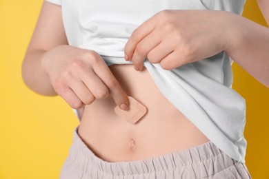 Photo of Woman applying contraceptive patch onto her belly on yellow background, closeup