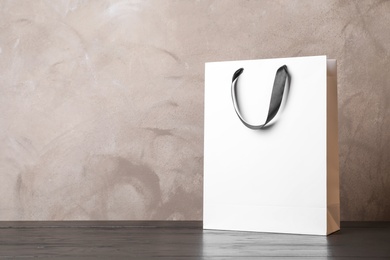 Photo of Paper shopping bag with handles on table against color wall. Mock up for design