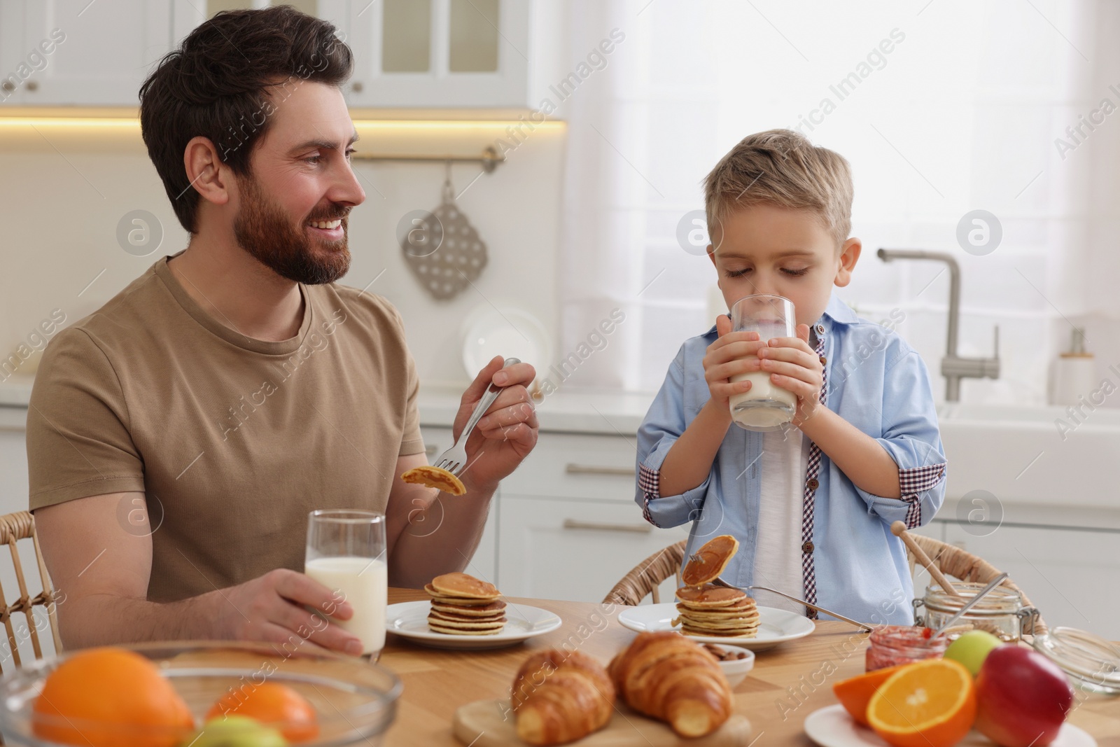 Photo of Father and his cute little son having breakfast at table in kitchen