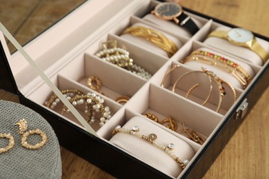 Photo of Elegant jewelry box with beautiful bijouterie and expensive wristwatches on wooden table, closeup