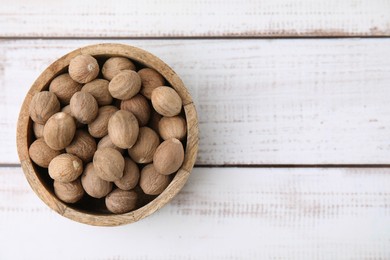 Photo of Whole nutmegs in bowl on light wooden table, top view. Space for text