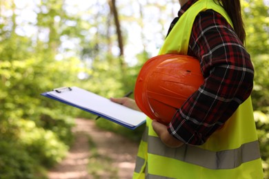 Photo of Forester with hard hat and clipboard examining plants in forest, closeup