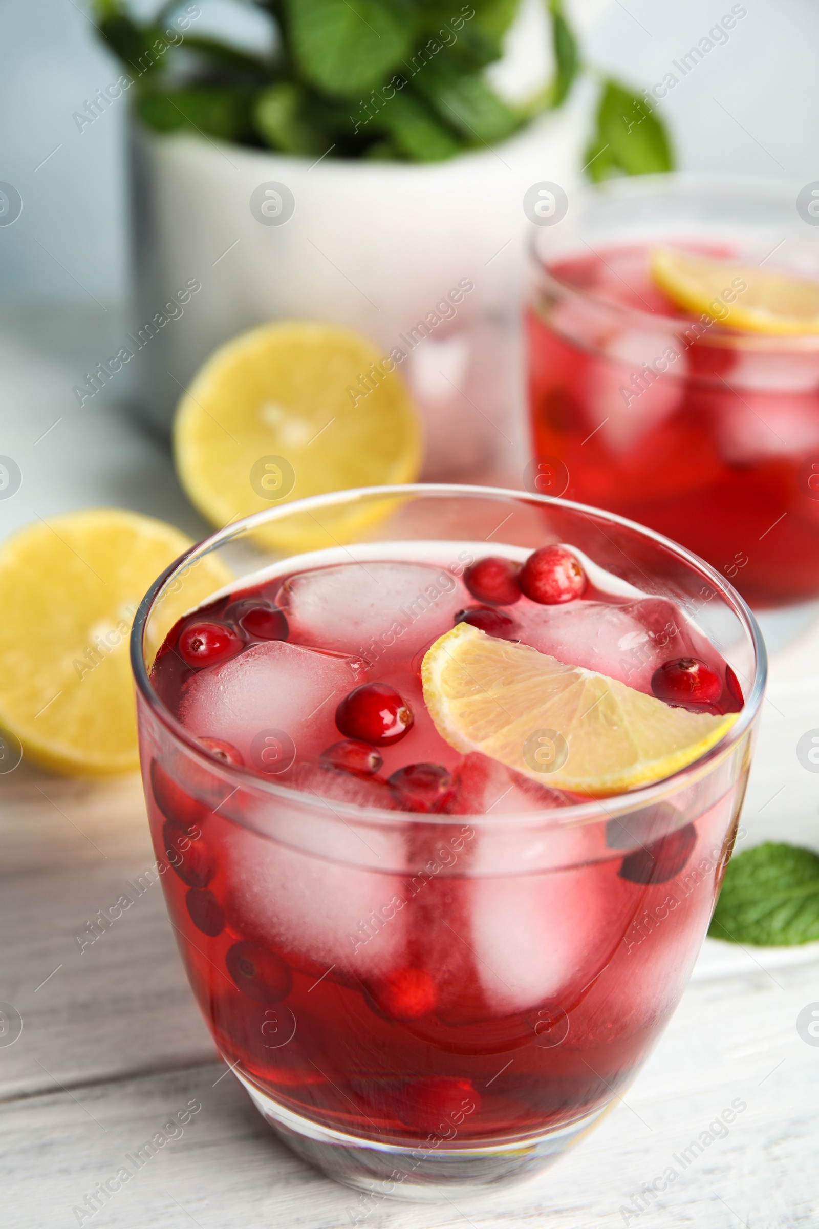 Photo of Tasty refreshing cranberry cocktail with lemon on white wooden table, closeup