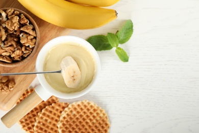 Photo of Dipping slice of banana into fondue pot with white chocolate on wooden table, top view. Space for text