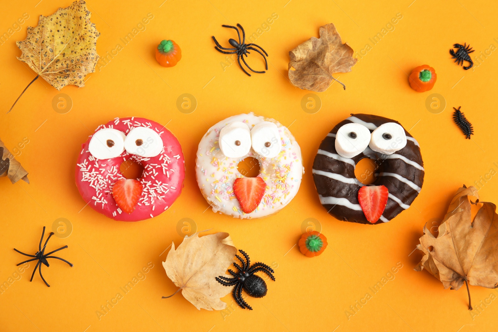 Photo of Delicious donuts decorated as monsters on orange background, flat lay. Halloween treat