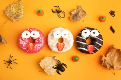 Delicious donuts decorated as monsters on orange background, flat lay. Halloween treat