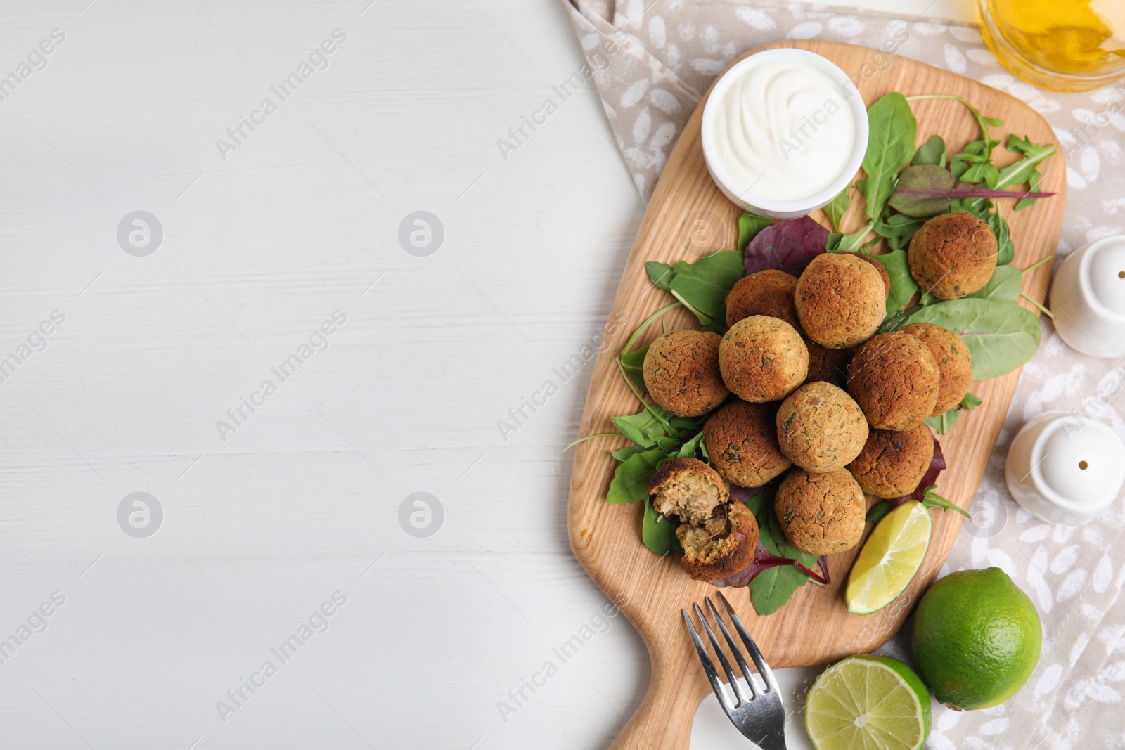 Photo of Delicious falafel balls with herbs, lime and sauce on white wooden table, flat lay. Space for text