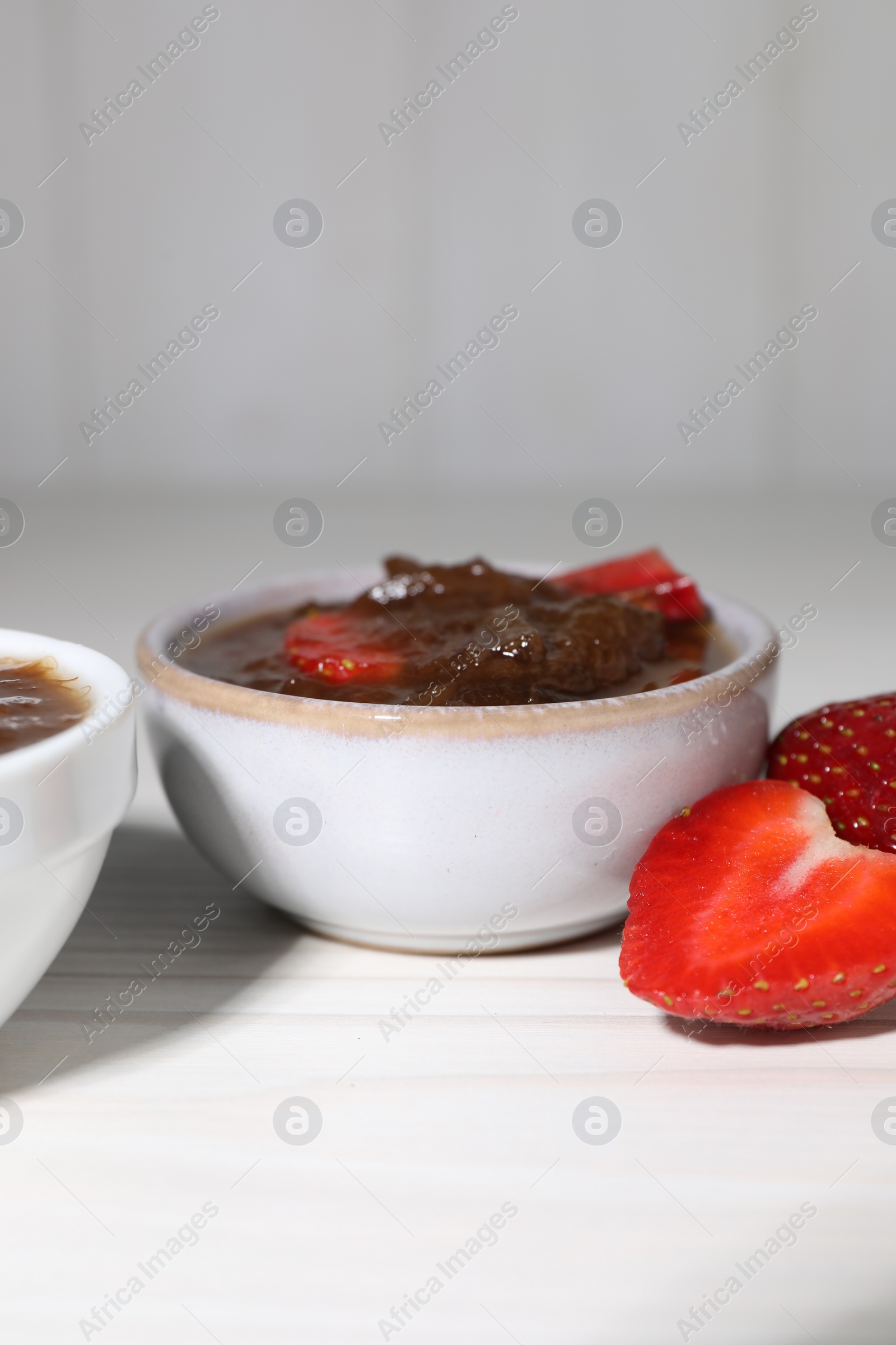 Photo of Tasty rhubarb jam and strawberries on white wooden table. Space for text