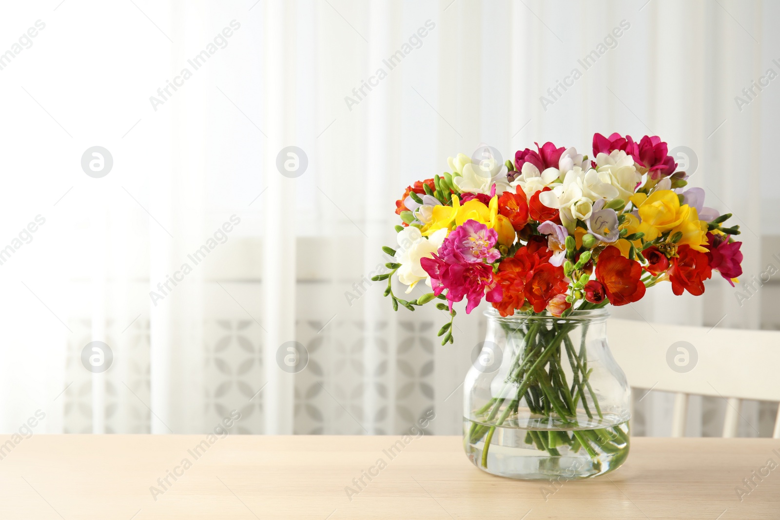 Photo of Vase with bouquet of spring freesia flowers on table in room