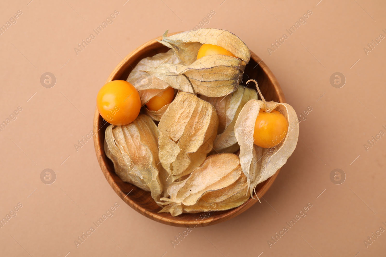 Photo of Ripe physalis fruits with calyxes in bowl on beige background, top view