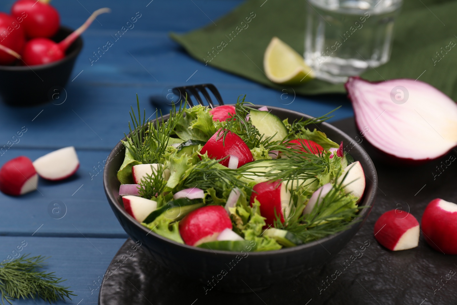 Photo of Tasty salad with radish in bowl on blue wooden table, closeup