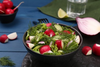 Photo of Tasty salad with radish in bowl on blue wooden table, closeup