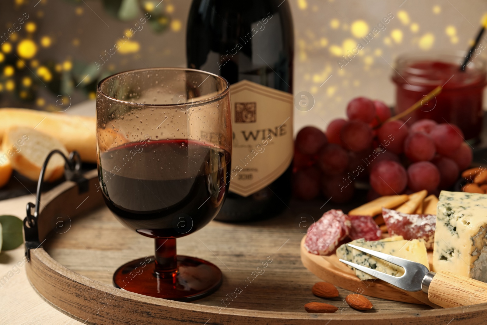 Photo of Glass of tasty red wine near bottle and delicious snacks on wooden table