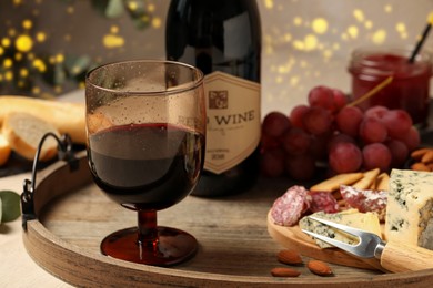 Photo of Glass of tasty red wine near bottle and delicious snacks on wooden table