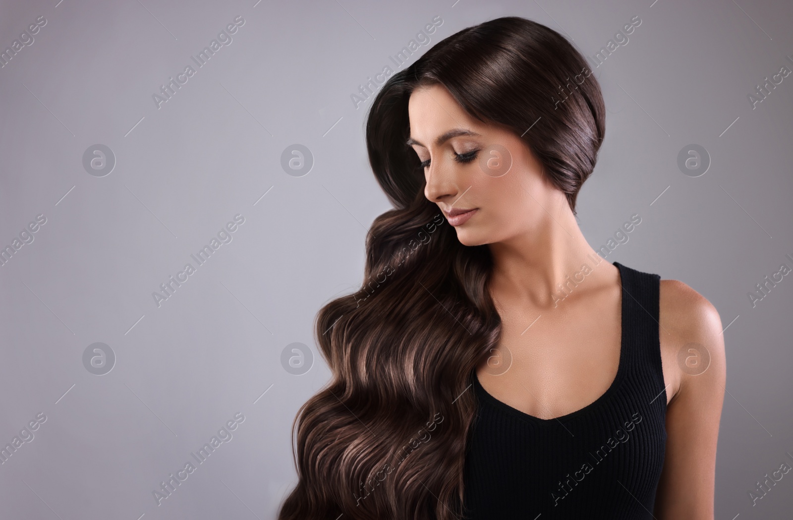 Image of Gorgeous woman with shiny wavy hair on grey background, space for text. Professional hairstyling