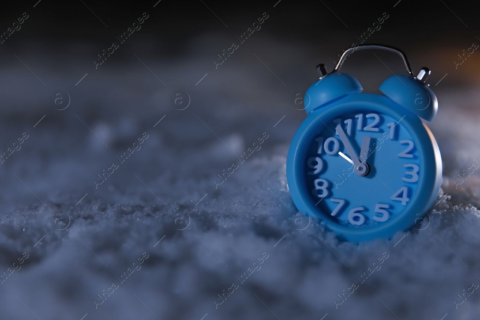 Photo of Blue alarm clock on white snow outdoors, space for text. Midnight countdown