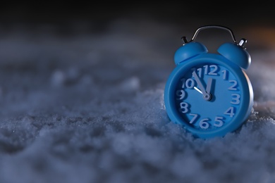 Photo of Blue alarm clock on white snow outdoors, space for text. Midnight countdown