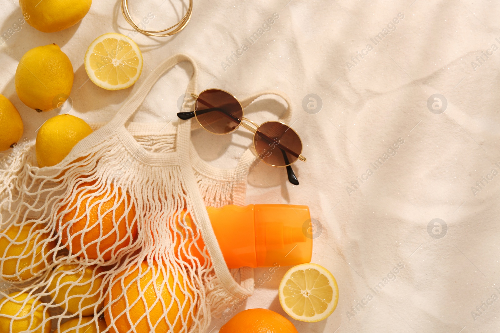 Photo of String bag with sunglasses, fruits and sunscreen on sand, flat lay. Space for text