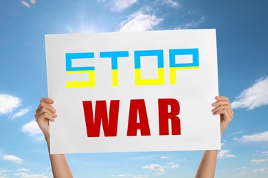 Woman holding poster with phrase Stop War against sky, closeup. Word Stop in colors of Ukrainian flag