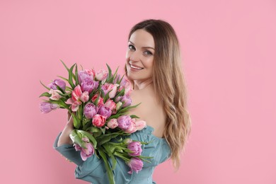 Happy young woman with bouquet of beautiful tulips on pink background