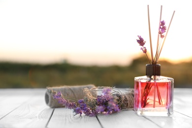 Photo of Reed air freshener and fresh lavender flowers on wooden table in field. Space for text