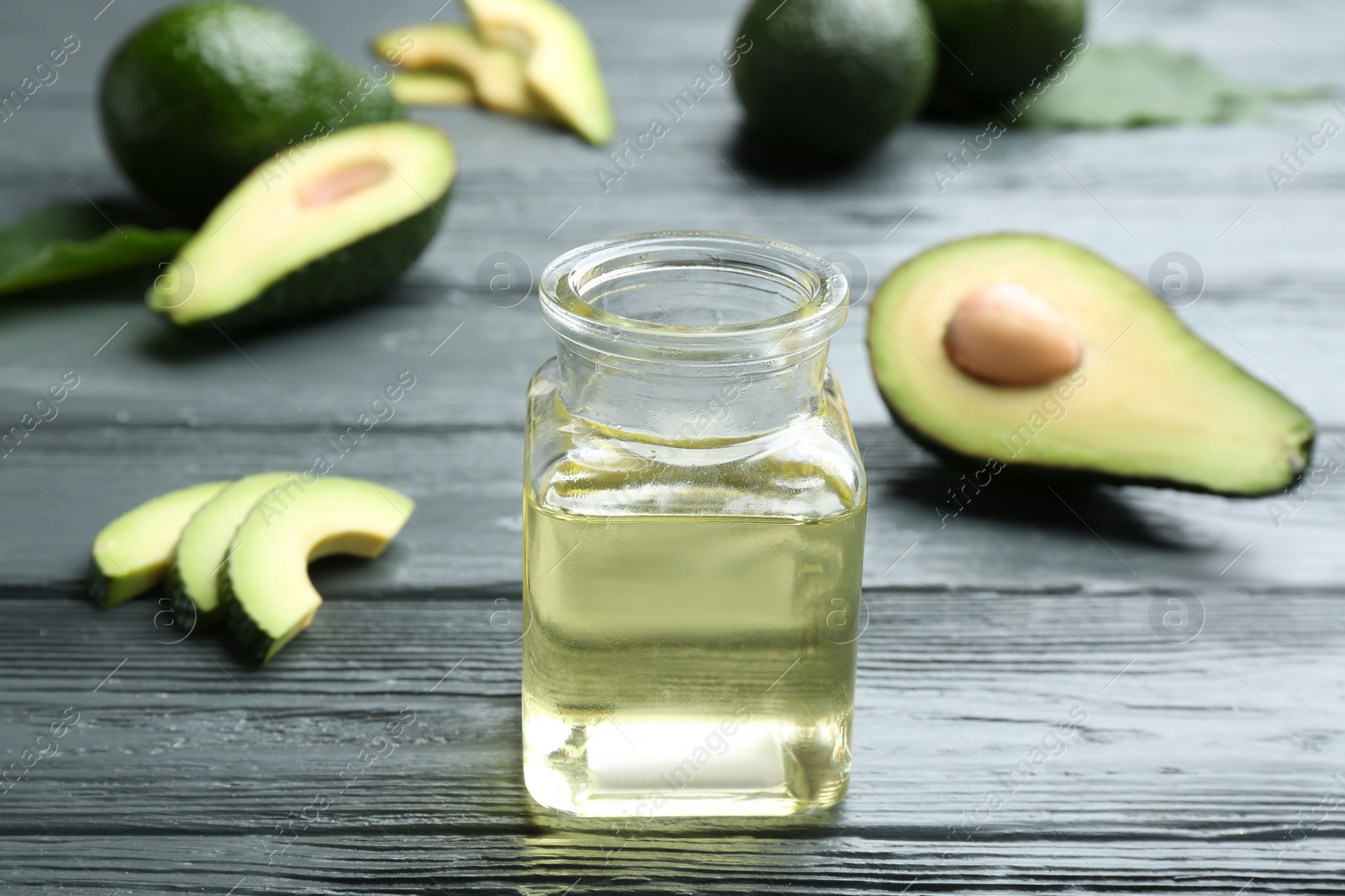 Photo of Jar of natural oil and avocados on grey wooden background