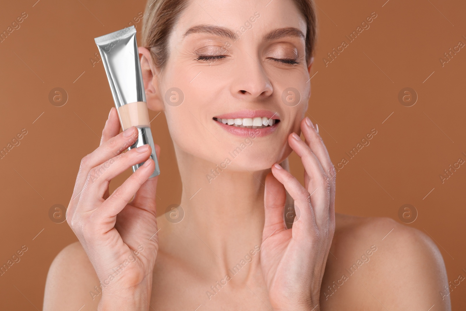 Photo of Woman holding tube of foundation on brown background