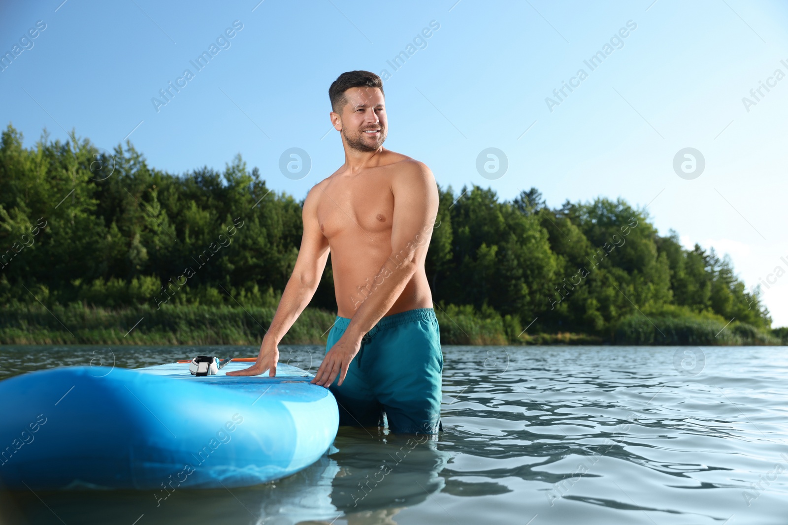 Photo of Man standing near SUP board in river water on sunny day