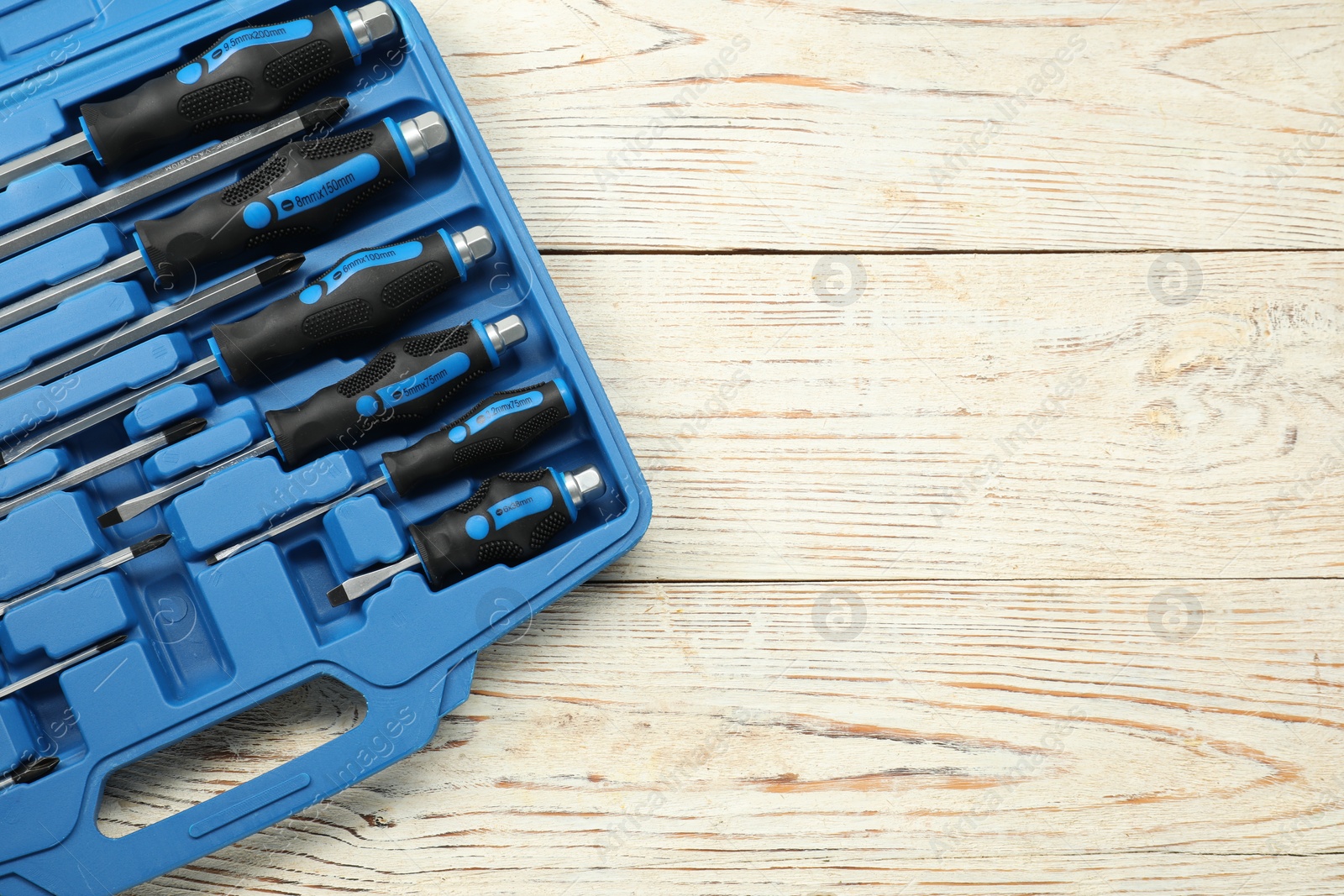 Photo of Set of screwdrivers in open toolbox on light wooden table, top view. Space for text