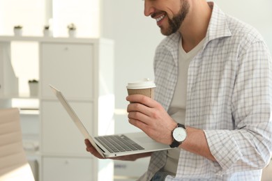Photo of Freelancer with cup of coffee working on laptop indoors, closeup