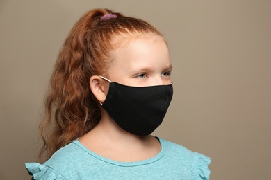 Preteen girl in protective face mask on brown background