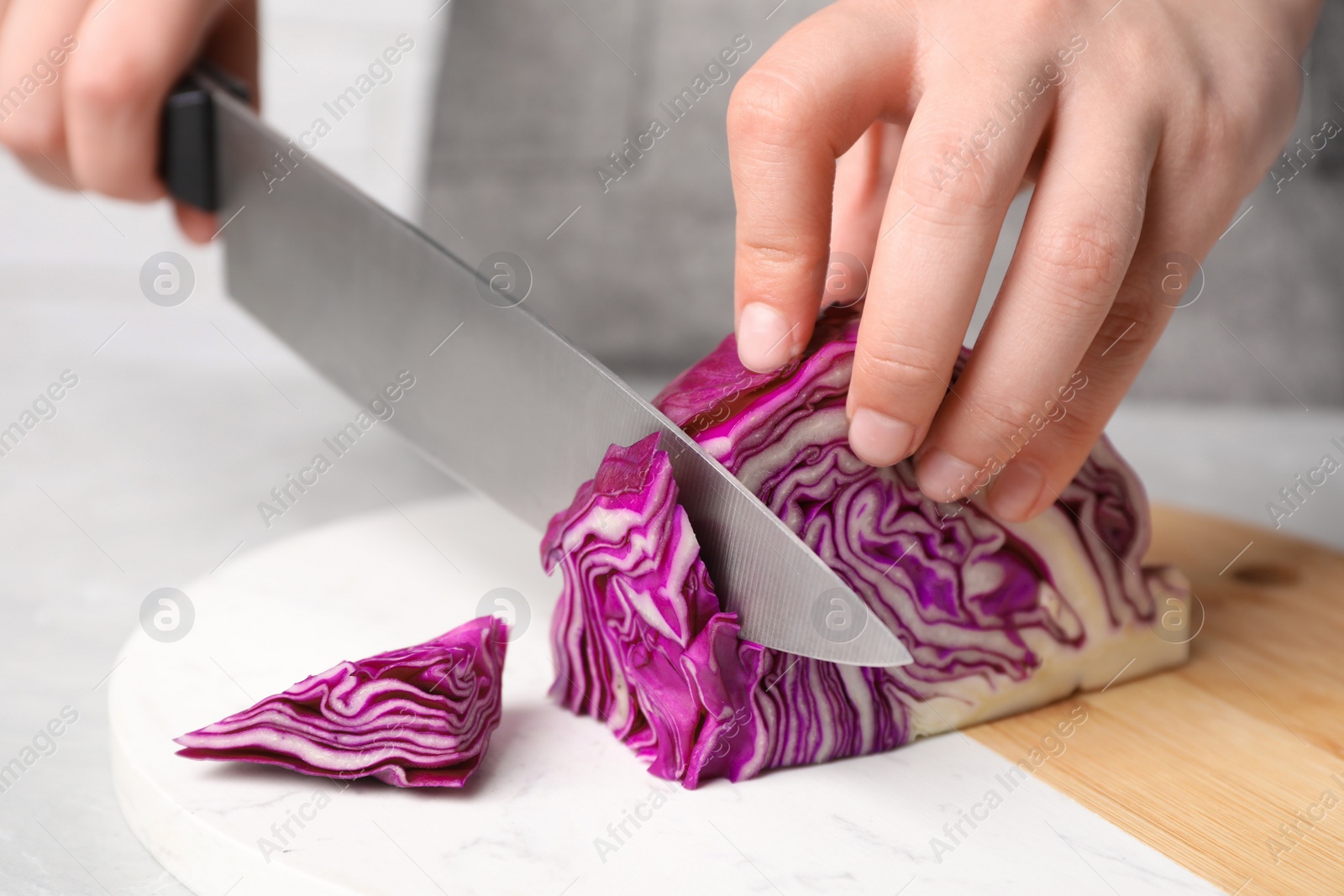 Photo of Woman cutting fresh red cabbage at table, closeup