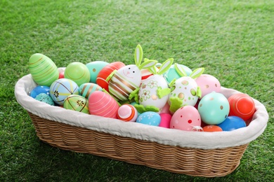 Photo of Many different Easter eggs in wicker basket on green grass