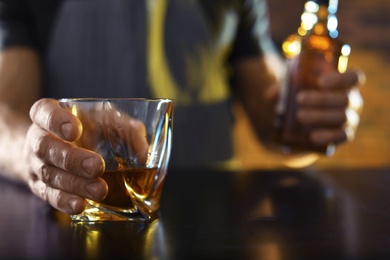 Photo of Bartender with glass and bottle of whiskey at counter in bar, closeup. Space for text