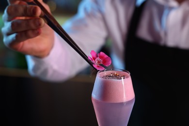 Photo of Bartender decorating fresh alcoholic cocktail with flower on blurred background, closeup
