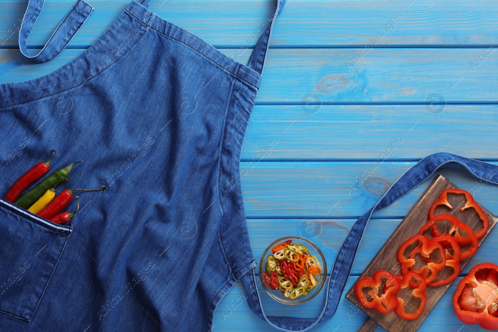 Photo of Flat lay composition with denim apron and fresh peppers on light blue wooden table. Space for text