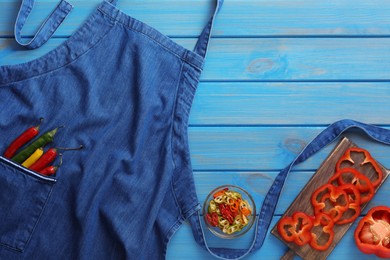 Photo of Flat lay composition with denim apron and fresh peppers on light blue wooden table. Space for text