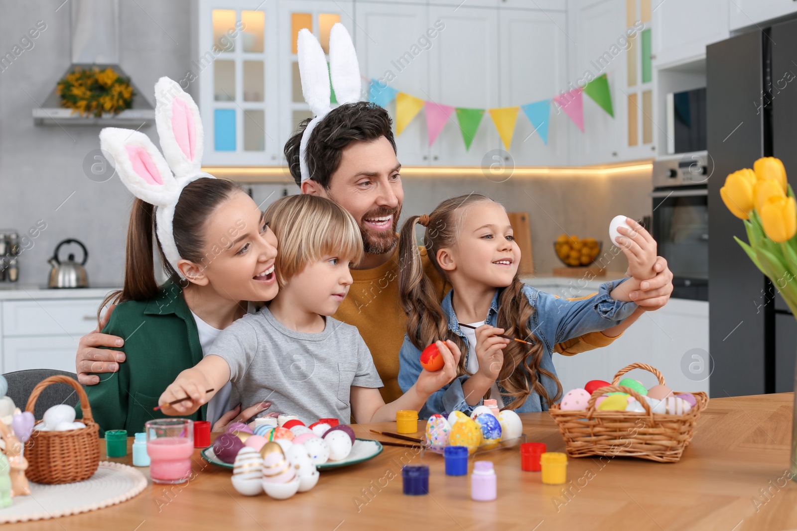 Photo of Happy family painting Easter eggs at table in kitchen