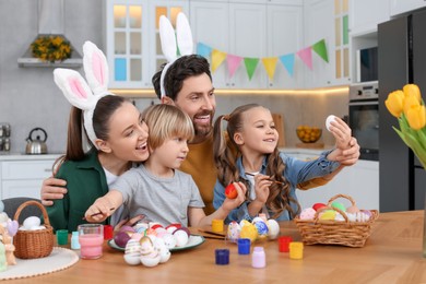 Photo of Happy family painting Easter eggs at table in kitchen