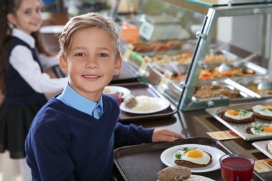 Photo of Cute boy near serving line with healthy food in school canteen