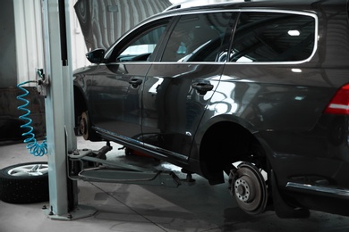 Photo of Modern car on hydraulic lift at automobile repair shop