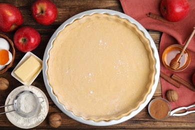Photo of Raw dough and ingredients for traditional English apple pie on wooden table, flat lay