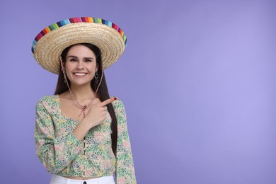 Photo of Young woman in Mexican sombrero hat pointing at something on violet background. Space for text