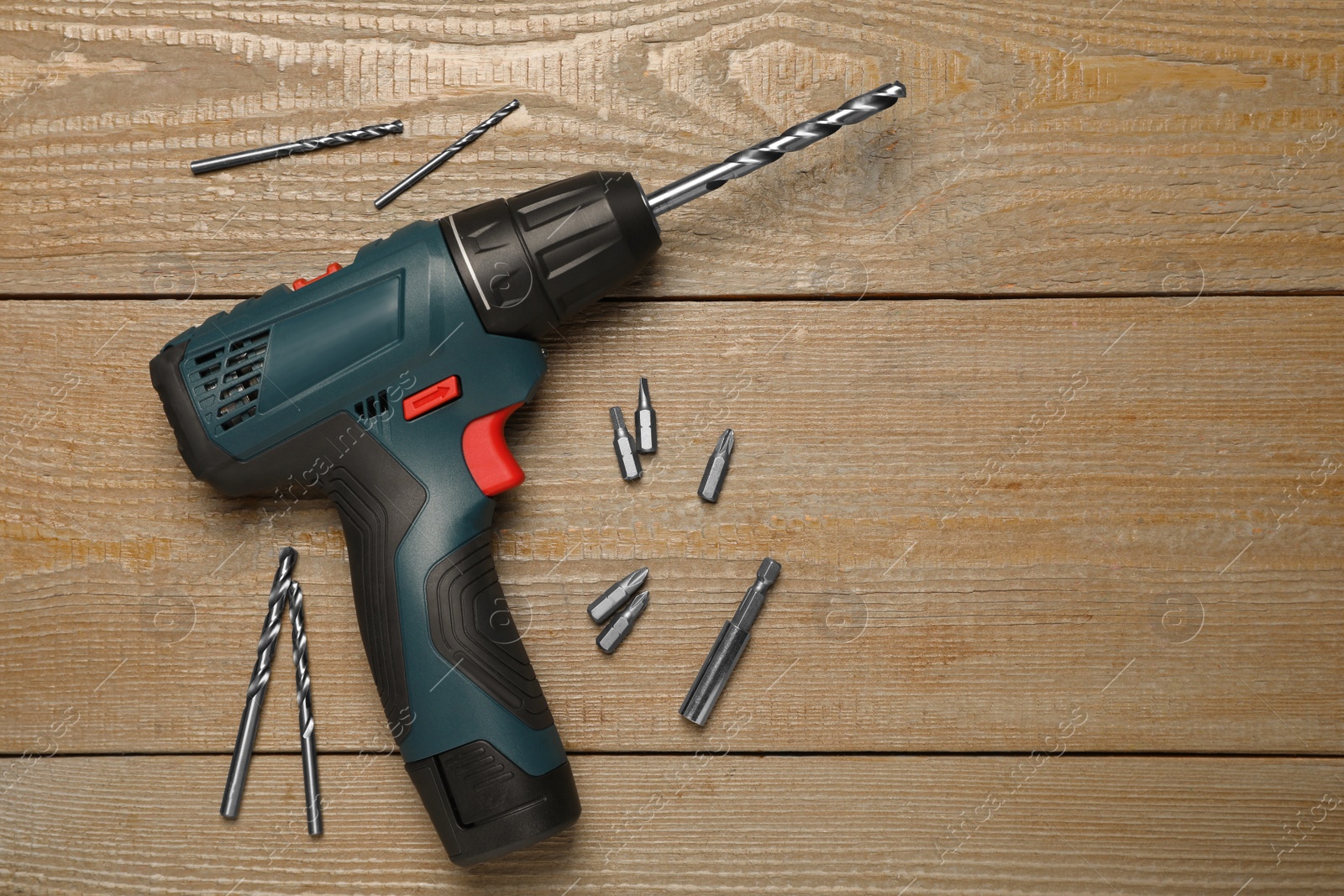 Photo of Modern electric power drill with different bits on wooden table, flat lay. Space for text