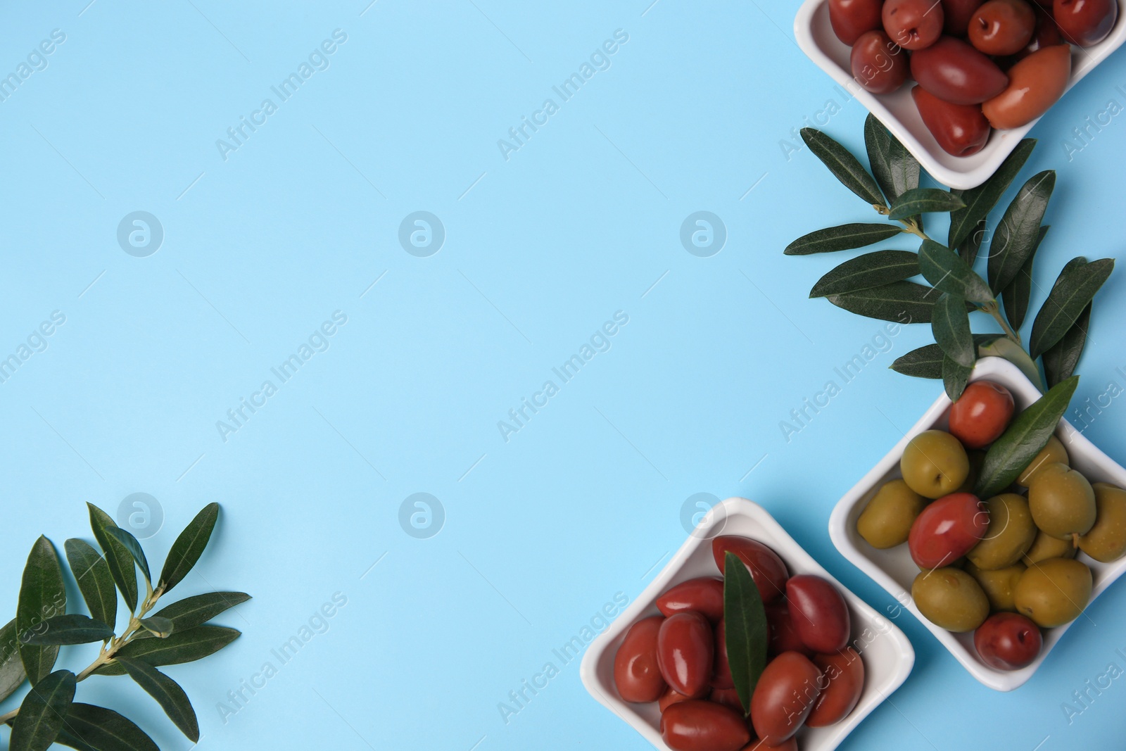 Photo of Different fresh olives and green leaves on light blue background, flat lay. Space for text