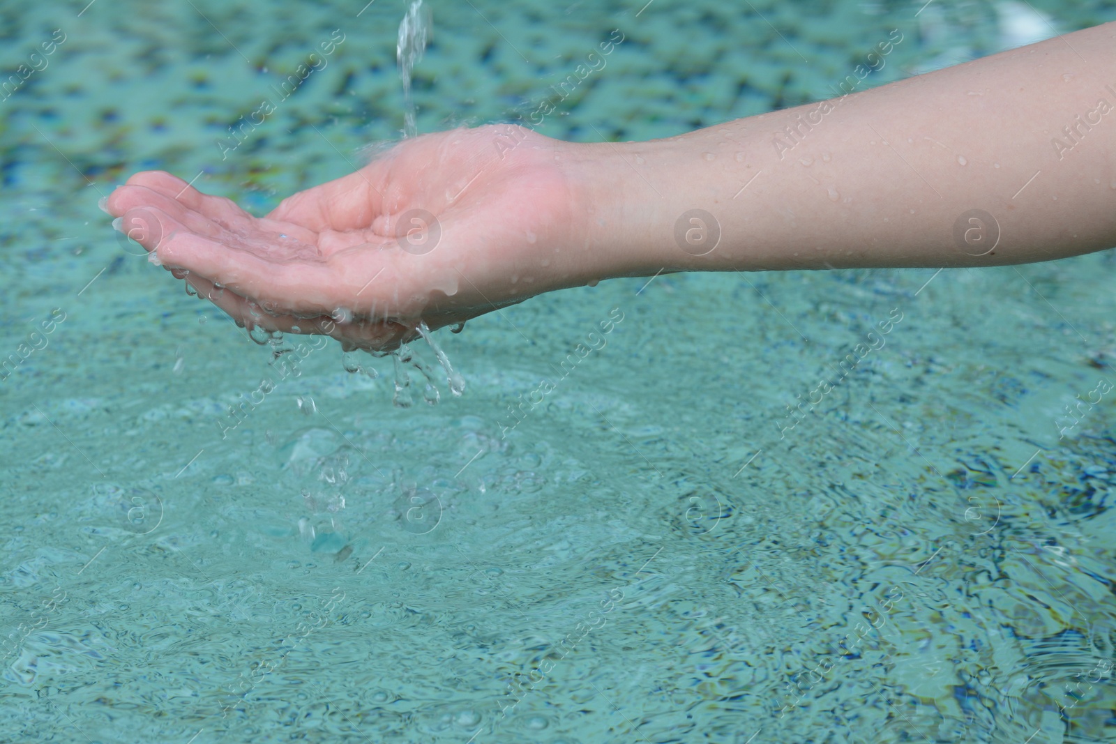 Photo of Water pouring into the girl's hand above pool, closeup