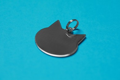 Silver metal pet tag in shape of cat with ring on light blue background, closeup. Space for text