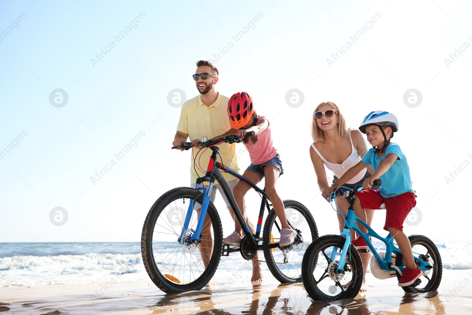 Photo of Happy parents teaching children to ride bicycles on sandy beach near sea